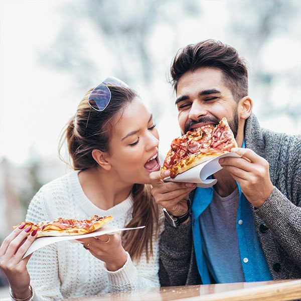 Frau will vom Pizzastück ihres Partners beißen - Heißhunger kann ein Schwangerschaftsanzeichen sein.